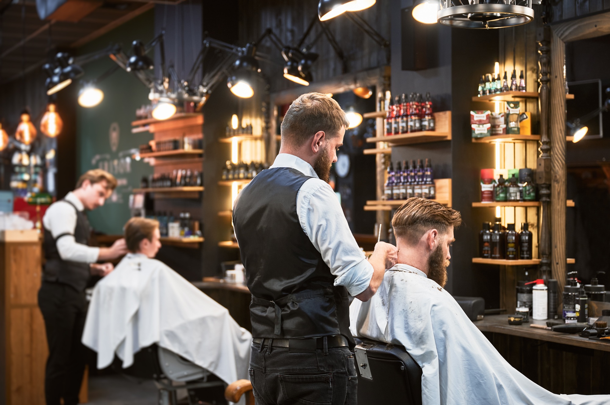 Professional barbers working on client hair in barbershop.
